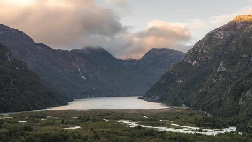 Vast valley with a lake surrounded by mountains and undergrowth under a cloudy sky
