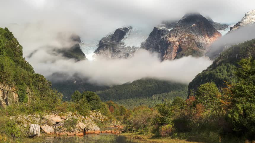 Sea of low clouds passing between greenish mountains on the edge of a lake