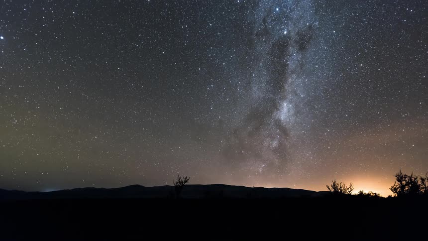 Rising sun tints starry night sky near the silhouetted mountains