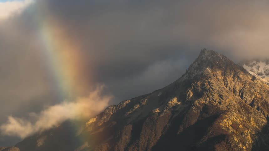 Dense cloud storm passing above mountain peaks with reflection of a rainbow