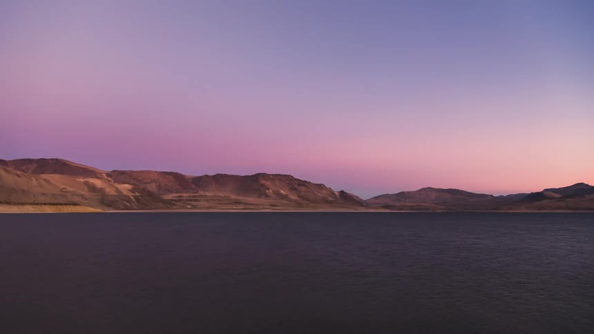 A mountainous region with a huge lake and it is daytime and then darkening