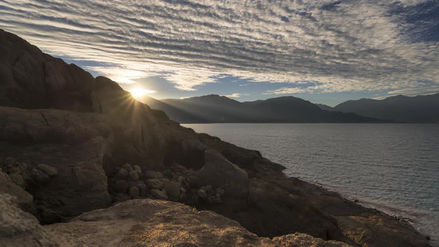 A rocky shore facing a bay of water and the day is passing quickly