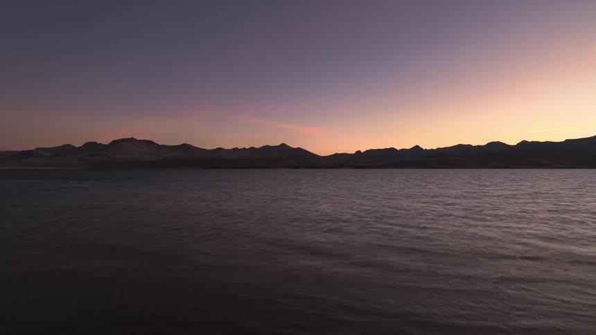 The sun is setting above the horizon of a body of water