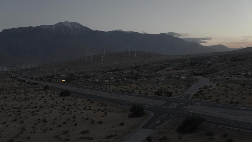 A wind-farm stands on a hill overlooking a desert road