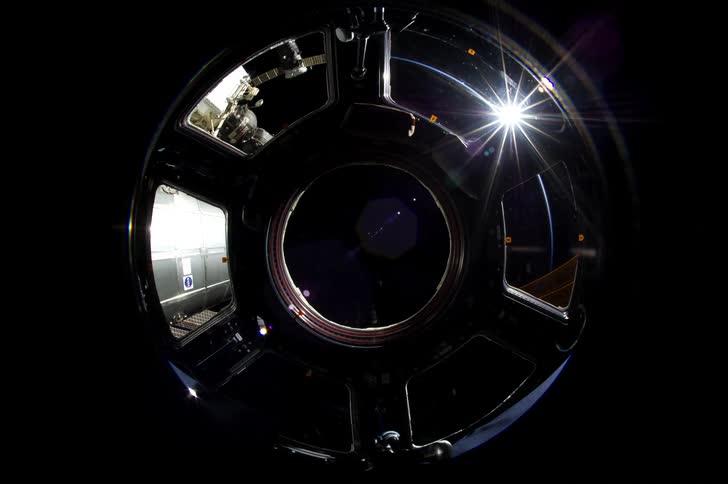 Space station orbits above the night side of earth while the sun illuminates a narrow arc of the earth surface