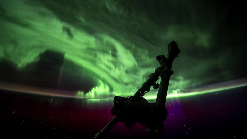 Space station orbits night side of earth while its exterior strut is silhouetted against the aurora borealis