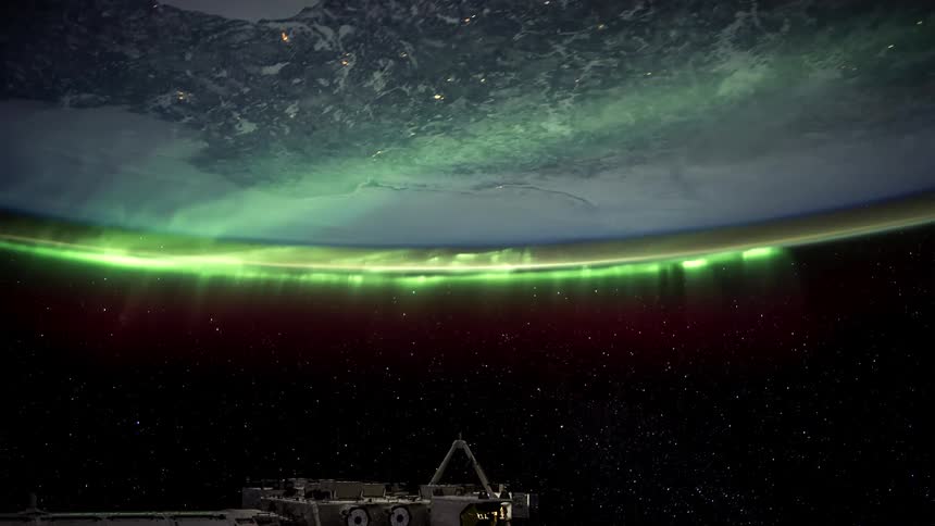 Space station orbits the earth while an aurora covers some of the atmosphere