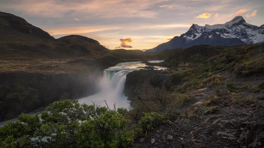 Landscape of a small waterfall surrounded by mountains and with a setting sun
