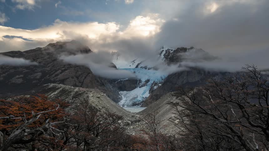 Glacier on mountain peaks with clouds passing by