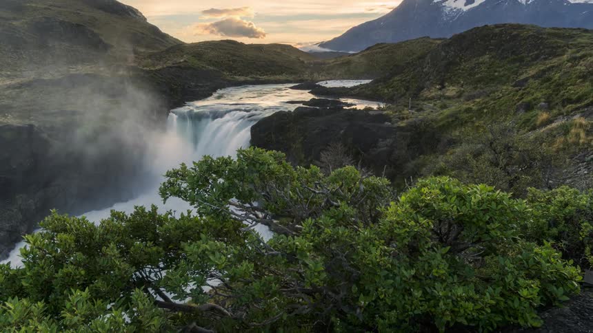 Aerial panorama of a waterfall with mountains on the horizon and cloudy sky