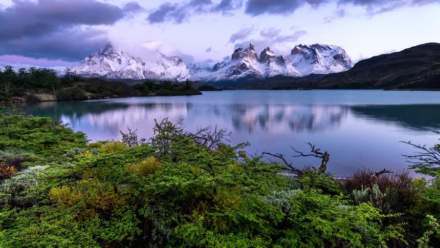 Landscape of a lake surrounded by snowy mountains and a reddish sunset sky