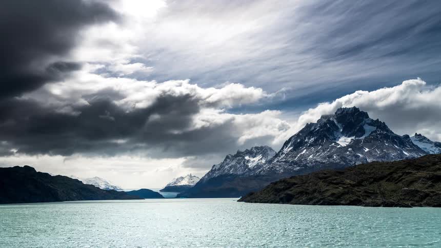 Nebulous cloud scenery above snowy mountains by a lake