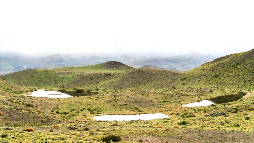 Serene natural landscape with three small lakes lined up in front of gentle hills and distant mountains