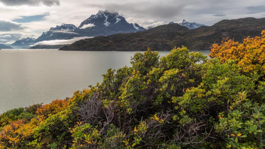 Lake surrounded by mountains and vegetation against a cloudy sky