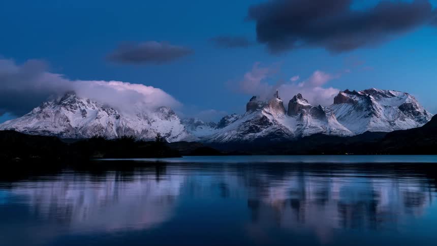 Lake that reflects snowcovered mountains in the background with dusk and the sky turning shades of purple and red