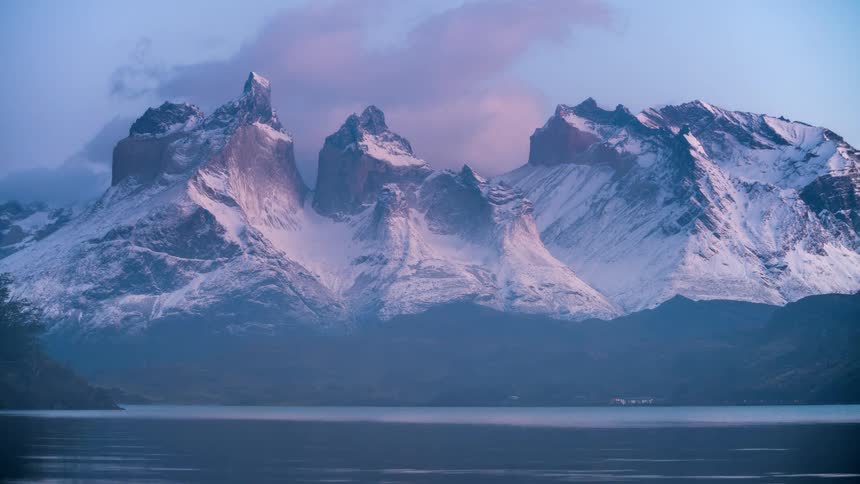 Rolling clouds over a snow covered mountain that is near a lake