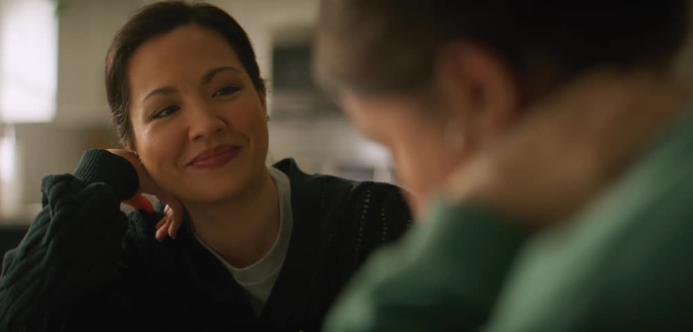 A woman smiles as she listens to another woman talking in the kitchen