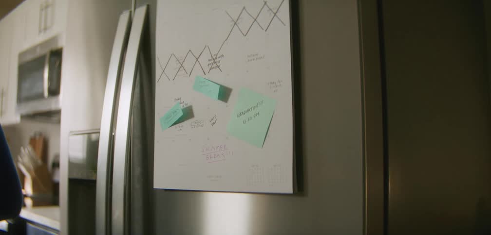 A woman writing notes on a notebook attached to the fridge door