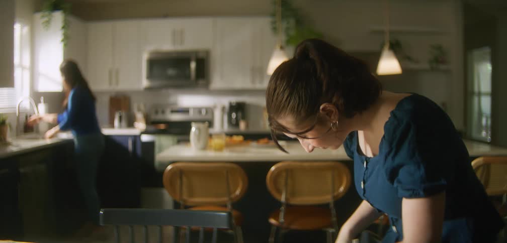 Student sets her backpack down on a chair and looks through it while talking to her mother in the kitchen