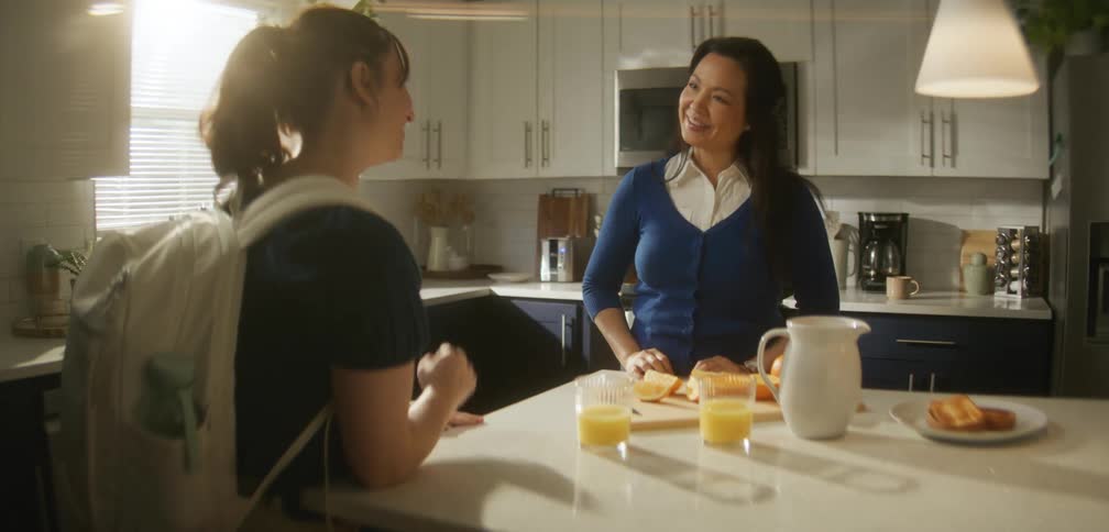 A woman smiles as she talks to a young female in a kitchen