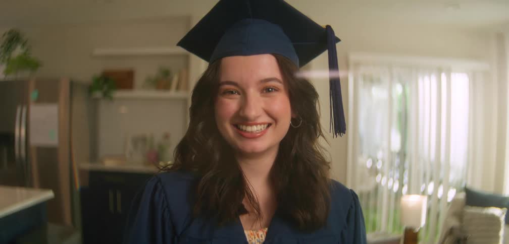 A young woman is smiling and wearing a graduation cap and gown