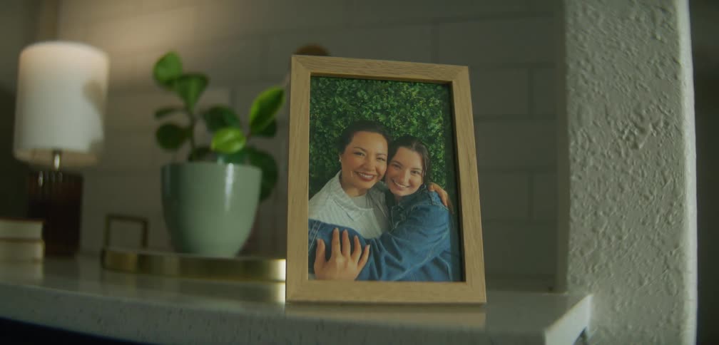 A framed photograph of two women hugging on a shelf at home