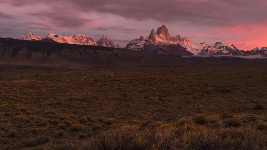 Natural landscape at dawn with distant mountains lit by the sun and a cloudy sky above