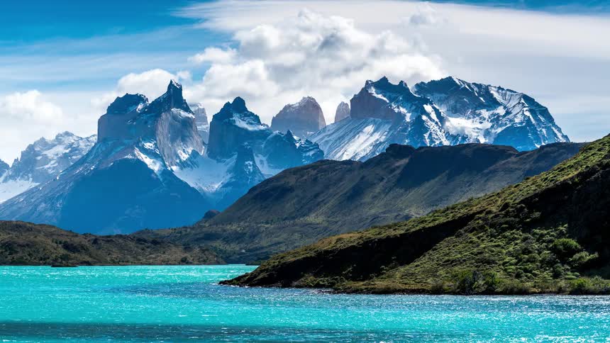 Natural landscape with a turquoise lake and towering mountains under a partly cloudy sky