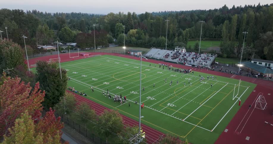 Low traverse over colorful fall foliage towards high school teams running a play during a Friday night football game