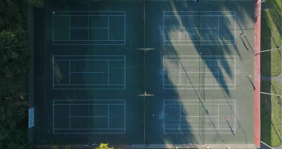 Top down view of six pairs of people playing on city park tennis courts