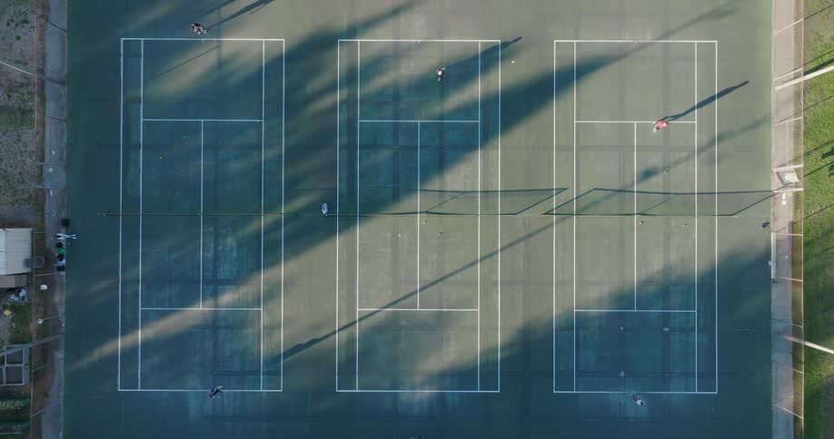 People play tennis on three parallel courts raked by morning sunshine