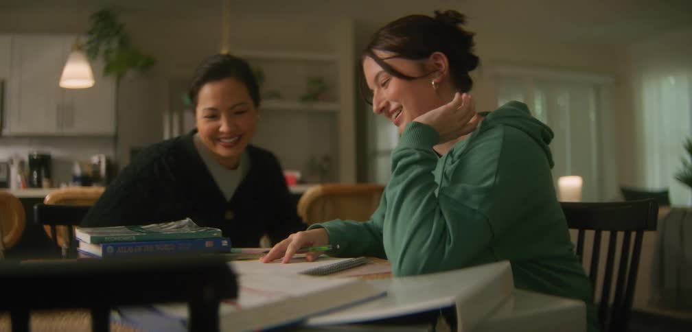 Mother sitting at the table with her daughter who is studying with books around her