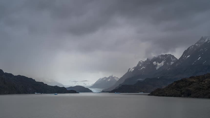 Scenery of snowy mountains by a lake on a day with dense clouds