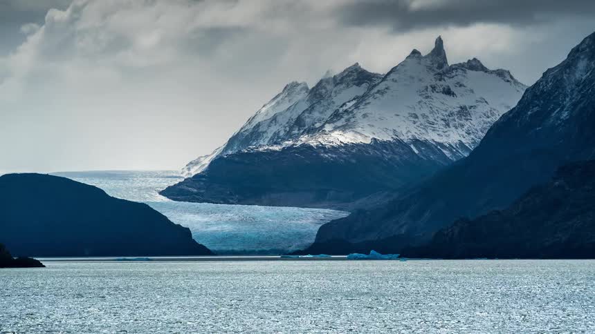 Landscape of mountains with snow and glaciers on the edge of a lake with clouds passing above