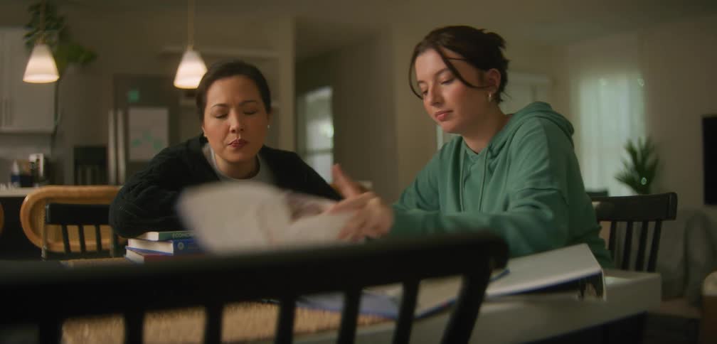Student reviews homework with her mother at the kitchen table