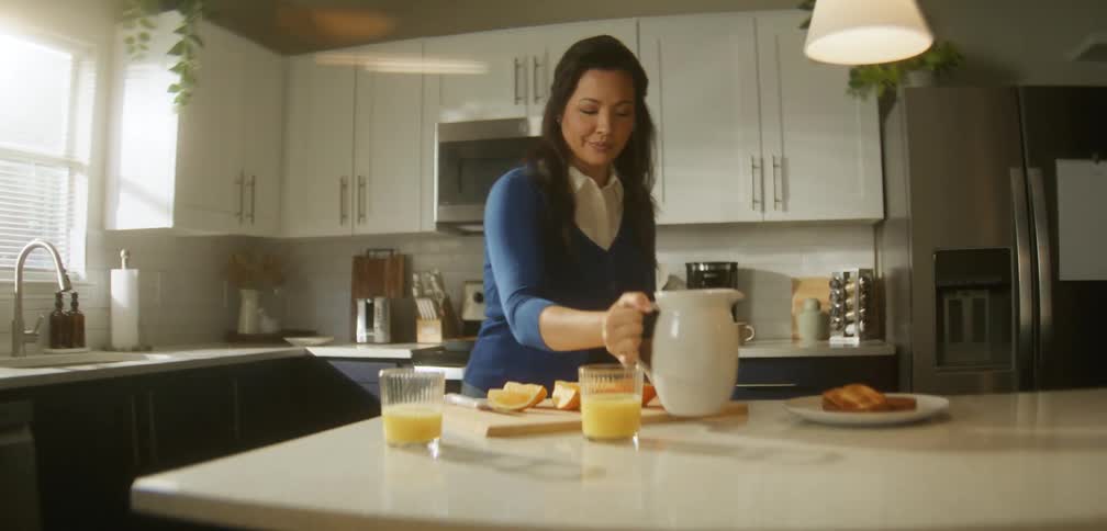 Woman placing a glass of orange juice and a pitcher on a kitchen counter