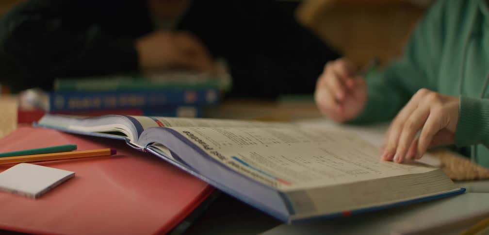 Two people are leafing through a book and pointing at it while they are reading