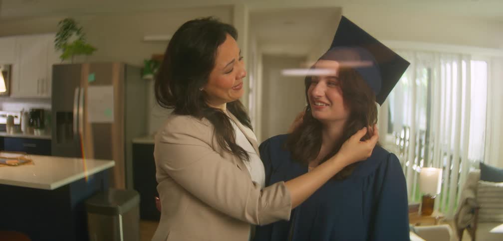 A mother looking at her daughter who is in a graduation cap and gown