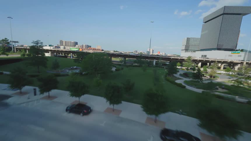 Traffic moving along city streets and a raised freeway pass park near downtown Dallas