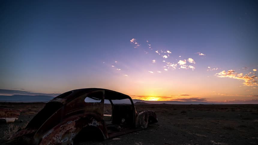 Wrecked and rusty car in a field with sunrise on the horizon