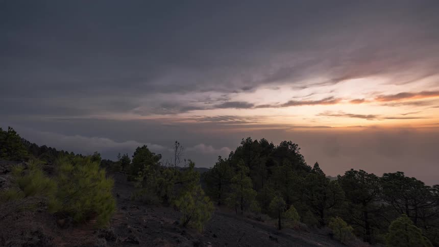 Dusk in a mountainous landscape where the low sun illuminates a cloudy sky and the moon appears on the horizon