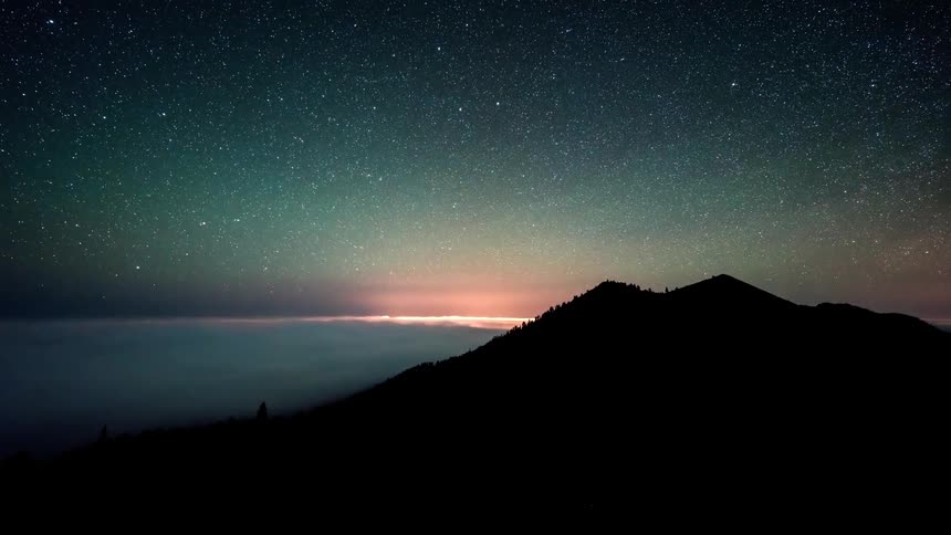 Landscape of a greenish mountain surrounded by a sea of clouds with the day getting dark and the sky becoming starry