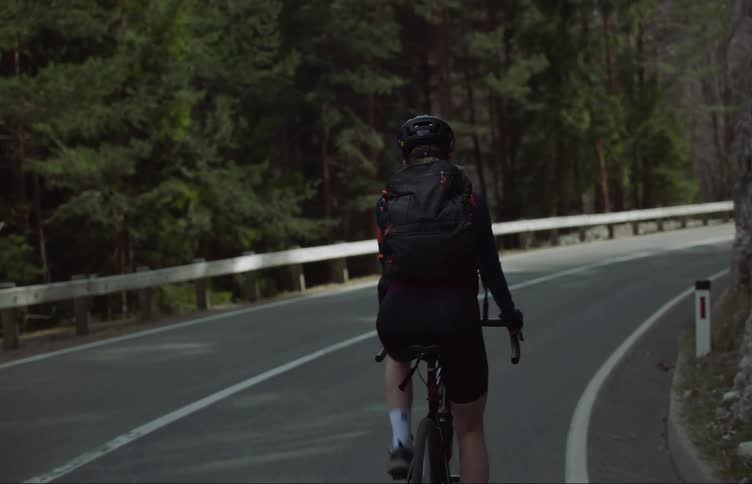 Woman bicycles down a hill next to a craggy mountain near the forest