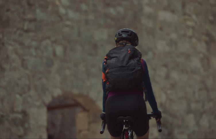 A woman is riding a bicycle and wearing a backpack