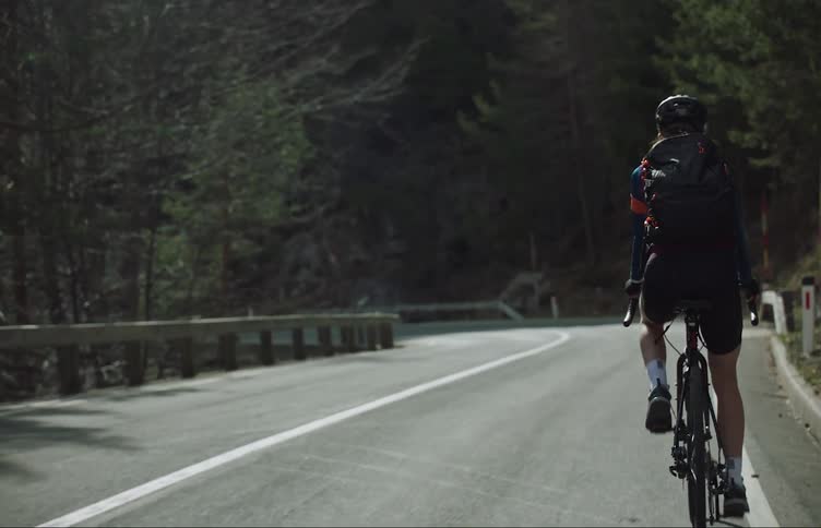 A cyclist rides down a paved road in a forested area