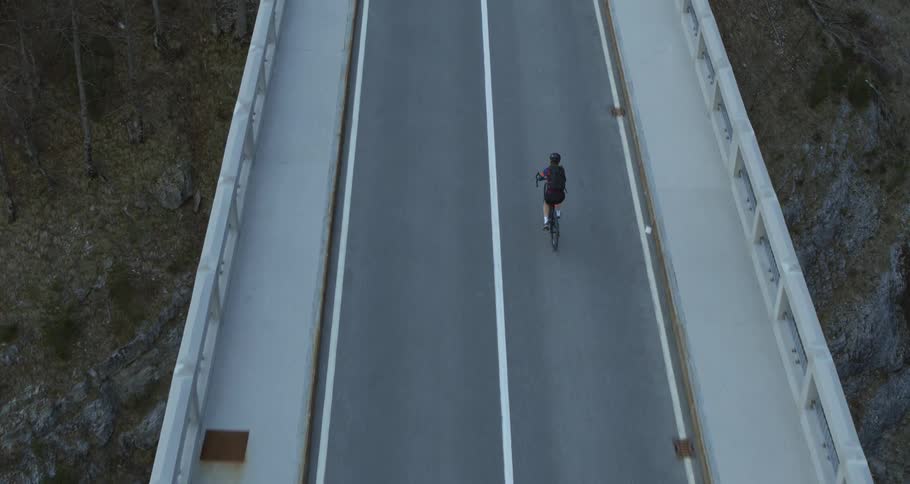 Bicyclist rides on an empty bridge overlooking the grassy and rocky hillside below
