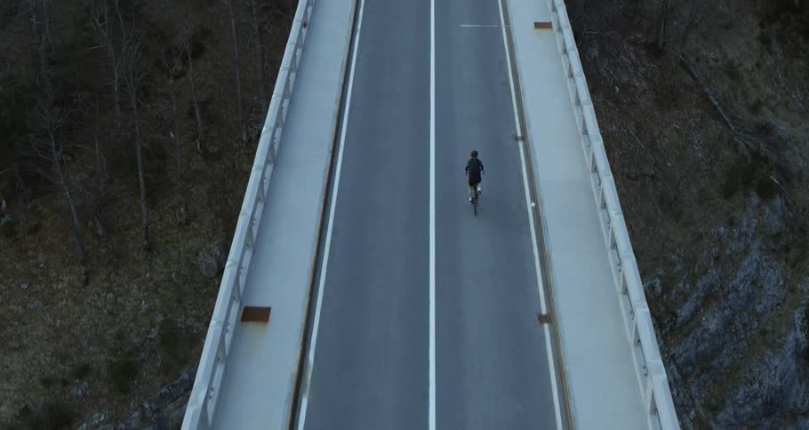 Bicyclist crossing a road on a bridge overlooking a treecovered hill