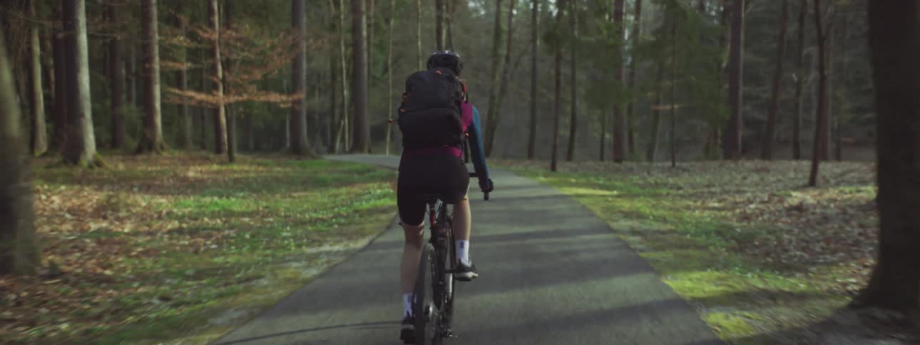 Woman bicycling on the street through the forest