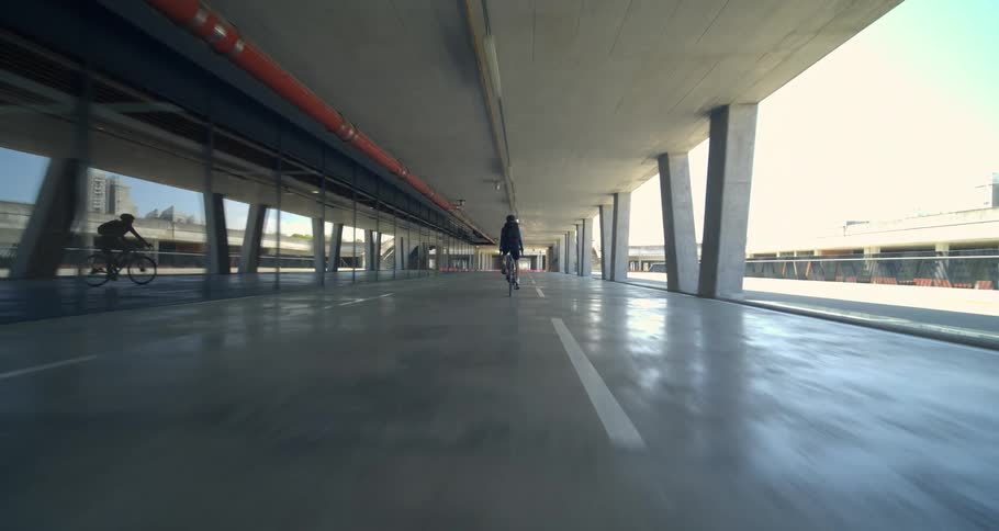 A person rides a bicycle through an overpass with a smoot concrete floor and ceiling