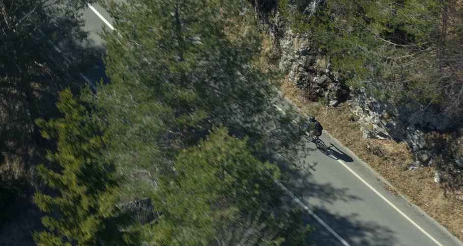 An aerial view of a cyclist driving on a winding road through the mountains